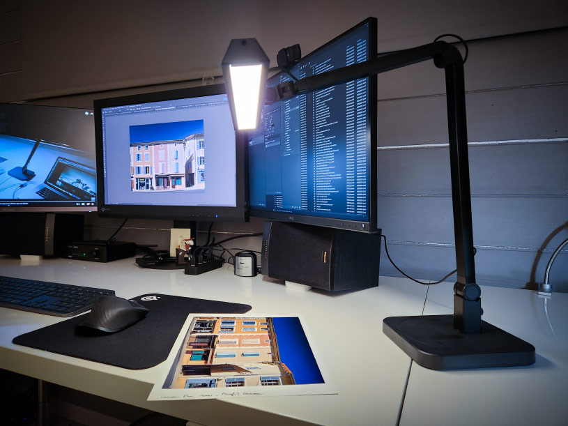 Mon bureau et son mur gris derrière les écrans de retouches photo et ma lampe Ilfolux
